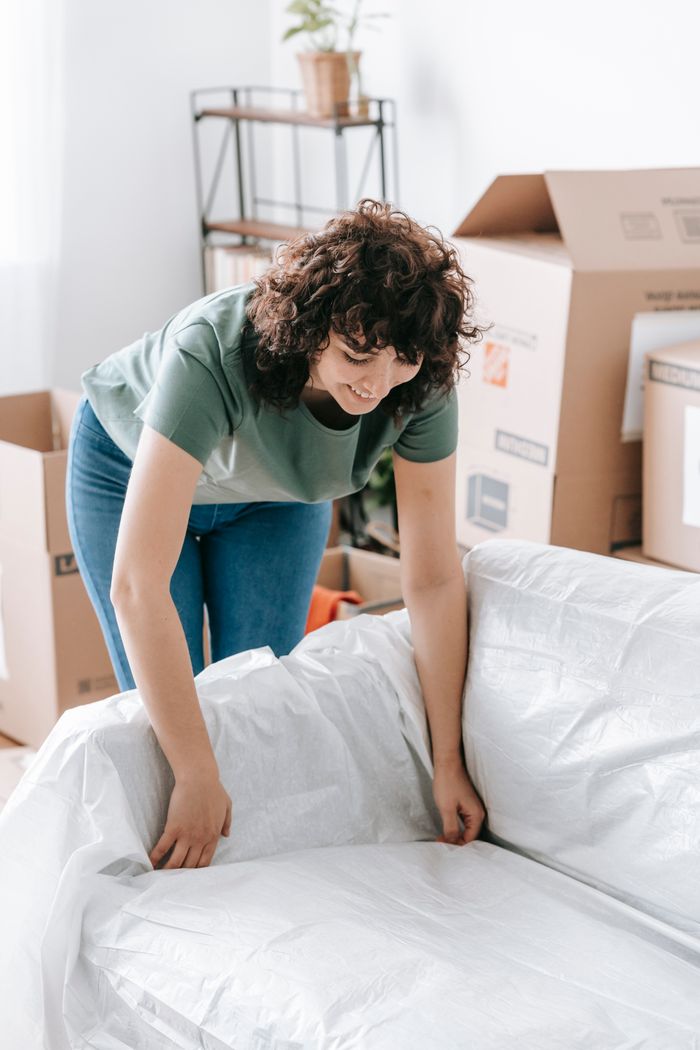 gallery-04 Woman wrapping a sofa with plastic for moving in a bright living room.